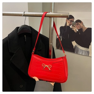 Détail du sac rouge en simili-crocodile avec un nœud en métal doré et texture brillante