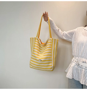 Detail of a large striped tote bag featuring a textured fabric and a metal logo plaque