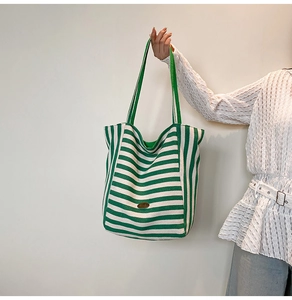 Close-up of green and white striped canvas tote bag with oval metallic logo and strap