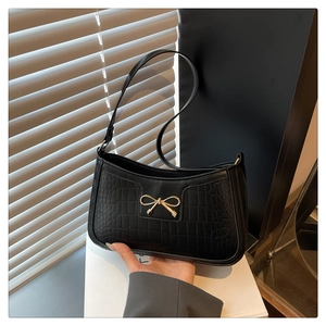 Detailed close-up of a black crocodile-embossed shoulder bag with a gold bow buckle