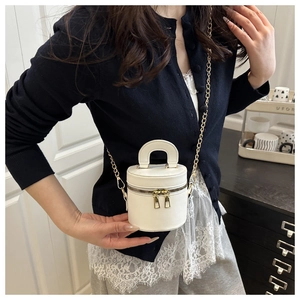 Close-up of white mini cylinder bag with dual zippers and gold chain strap on model