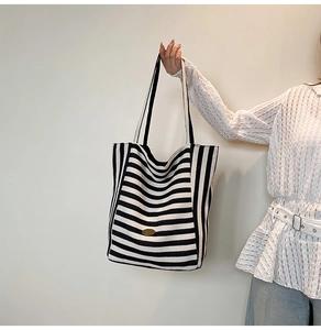 Detail of black and white striped tote bag showing the metal logo and wide handle strap