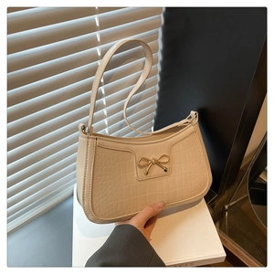 Détail du sac beige texture crocodile avec nœud doré et bandoulière fine élégante