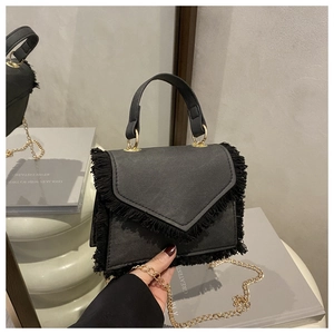 Détail d'un sac enveloppe noir à franges avec chaîne métallique et texture tissée