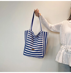 Detail of blue and white striped canvas tote bag featuring an oval metal logo plaque