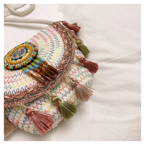 Detail of bohemian woven crossbody bag featuring colorful embroidery and long pink tassels