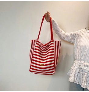 Detail of red and white striped canvas tote bag with golden metal logo and long shoulder strap