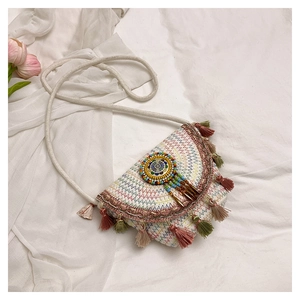 Détail du sac selle bohème avec pompons colorés, disque perlé et texture en tissu tissé