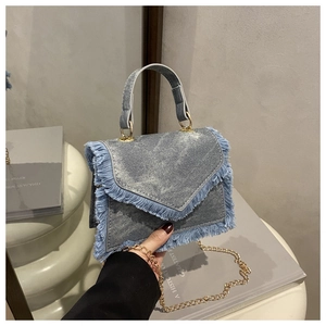 Détail du sac bandoulière en denim bleu clair avec bords effilochés et chaîne dorée