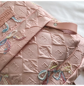 Close-up of pink quilted fabric with diamond pattern and colorful embroidery on the bag
