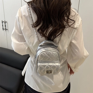 Chic silver quilted mini backpack with metal chain straps and turn-lock closure on model
