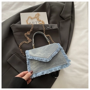 Détail d'un sac à main en jean bleu clair avec franges et chaîne dorée sur un blazer