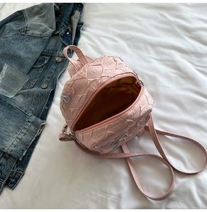 Detail of pink quilted mini backpack with woven charm on a white aesthetic background