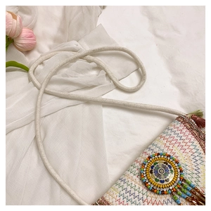 Detail of ethnic woven crossbody bag with colorful embroidery and beaded floral pendant