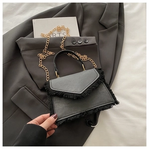 Détails des franges noires et de la bandoulière en chaîne dorée sur un petit sac moderne