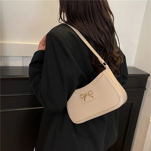 Sac bandoulière blanc crème à motif crocodile avec nœud doré porté sur une veste noire