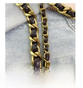 Dettaglio della catena in metallo dorato intrecciata con pelle marrone su denim