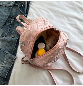 Pink quilted mini backpack showing inner capacity with cosmetics on denim fabric