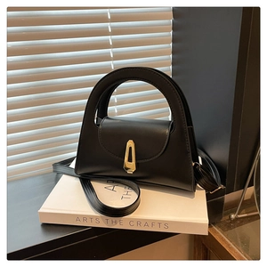 Detail of a black structured handbag with gold geometric clasp and long strap on books