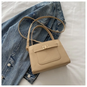 Detail of light beige small square bag showing golden twist lock and textured finish