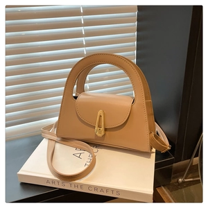 Detail of minimalist leather handbag featuring a half-moon handle and gold metal lock