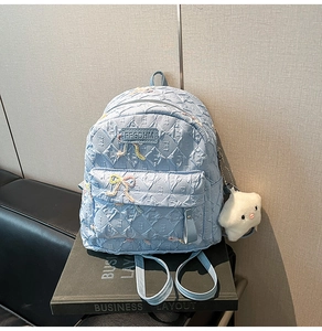 Close-up of light blue quilted backpack with embroidered bows and plush charm detail