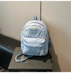 Detail of light blue quilted nylon backpack featuring colorful sequin embroidery and logo