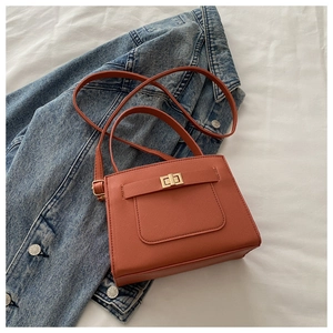 Detail view of brick red crossbody bag with golden turn-lock on blue denim jacket