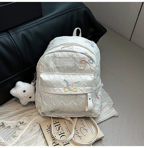 Close-up of white quilted backpack with glitter bows and a plush cloud charm detail