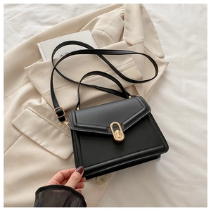Détail du sac carré en cuir noir avec fermoir doré posé sur un blazer beige chic