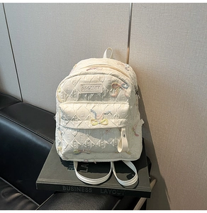 Detailed view of white quilted backpack with embroidery bows on business props