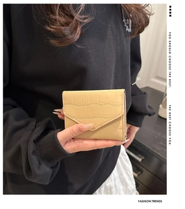 Dettaglio del portafoglio beige con trama a coccodrillo e patta a busta in mano