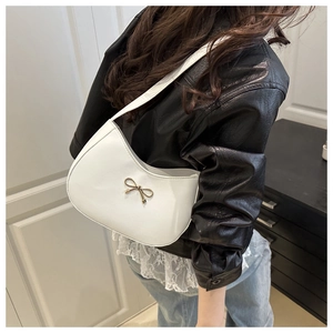 Detailed view of white crescent shoulder bag with golden bow buckle on black leather jacket