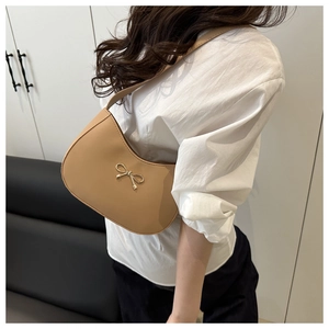 Detail of hobo bag featuring a gold bow ornament and smooth camel faux leather texture