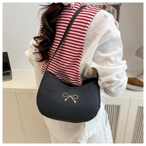 Detail view of a black hobo bag with gold bow ornament worn by a model in casual style