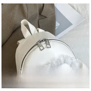 Detailed close-up of smooth metal zippers and lace trim on a white leather backpack
