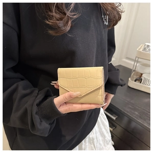Dettaglio di un portafoglio pieghevole beige con stampa coccodrillo in mano a modella