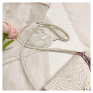 Detailed close-up of woven shoulder bag with purple ethnic embroidery and cream cotton tassels