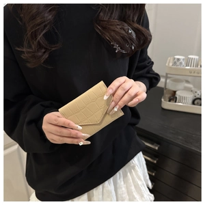 Dettaglio mini portafoglio beige con motivo a coccodrillo tenuto da una modella casual