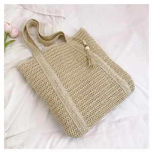 Detail of beige hollow straw tote bag with tassels on a soft white background