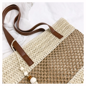 Detail of hollow woven straw beach bag featuring brown PU leather handle and beaded charm