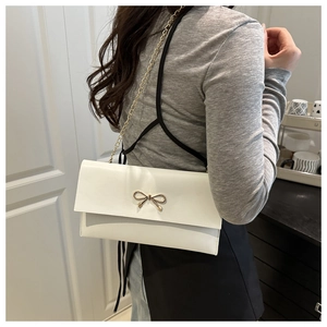 Close-up of a white rectangular crossbody bag with a golden metal bow and chain strap
