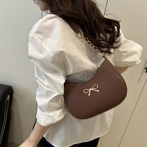 Brown half-moon underarm bag with golden bow ornament and leather chain strap on a model