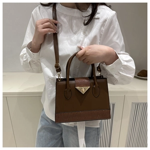 Detail of dark brown leather crossbody bag with textured patchwork and golden triangle lock