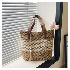 Detail of color-block straw tote bag with brown leather handles and decorative fringe tassel