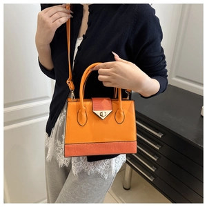 Orange crossbody bag with crocodile texture and V-shaped lock shown on model indoors
