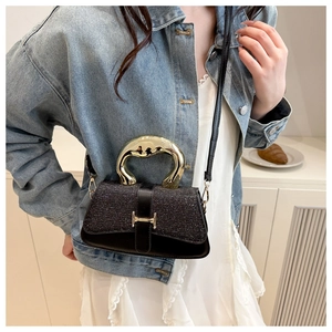 Detail view of glossy black glitter handbag with golden metal H-clasp and round handle