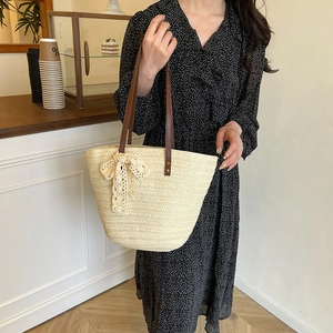 Beige straw tote bag with brown leather straps and a delicate lace bow charm detail