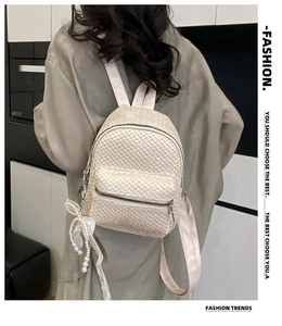 Detail of a beige woven straw backpack with pearl bow charm on a model's back