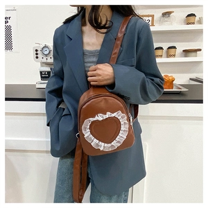 Detail of dark brown mini backpack featuring white lace heart trim and PU leather texture